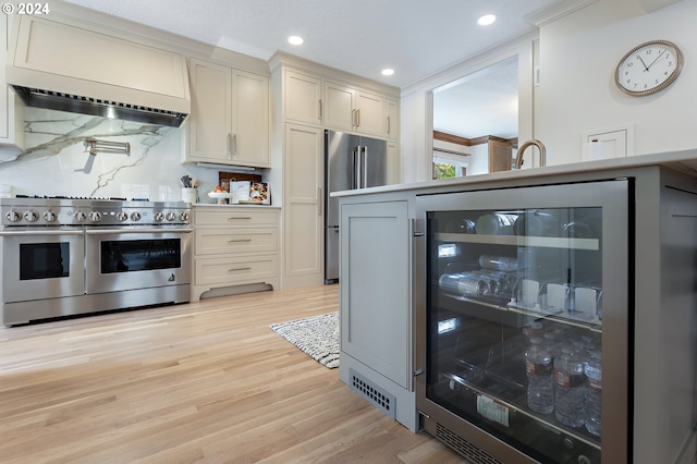 kitchen with premium appliances, light countertops, light wood-style flooring, beverage cooler, and wall chimney exhaust hood