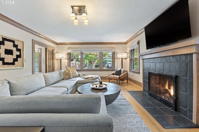 living room with ornamental molding, a textured ceiling, wood finished floors, a tile fireplace, and baseboards