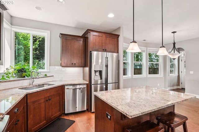 665 NE Skidmore St, Portland, OR 97211 - kitchen featuring appliances with stainless steel finishes, light wood finished floors, light stone counters, backsplash, and a kitchen breakfast bar