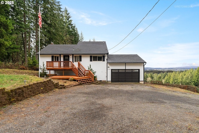 ranch-style home featuring driveway, an attached garage, a deck, and roof with shingles