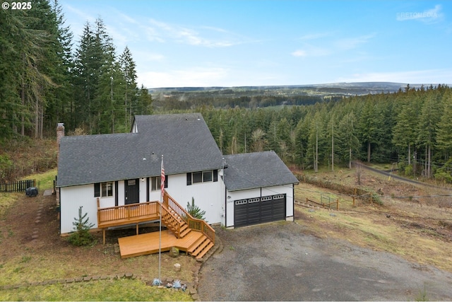 view of front of property featuring roof with shingles, an attached garage, fence, a wooded view, and driveway