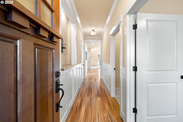 hallway with crown molding, a decorative wall, a wainscoted wall, and light wood finished floors