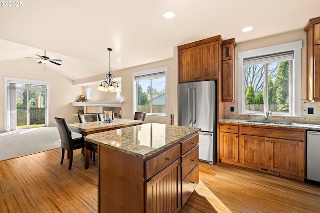 kitchen featuring lofted ceiling, light wood-style flooring, stainless steel appliances, brown cabinets, and a center island