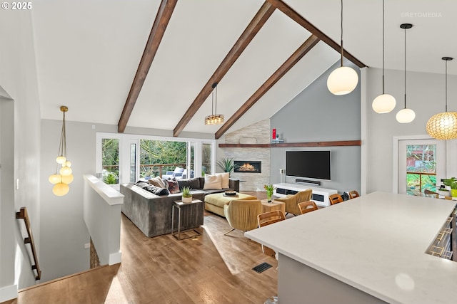 living room featuring beam ceiling, light wood-type flooring, high vaulted ceiling, and a large fireplace