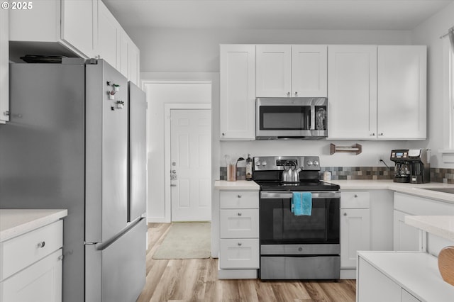 kitchen with stainless steel appliances, white cabinetry, and light hardwood / wood-style flooring