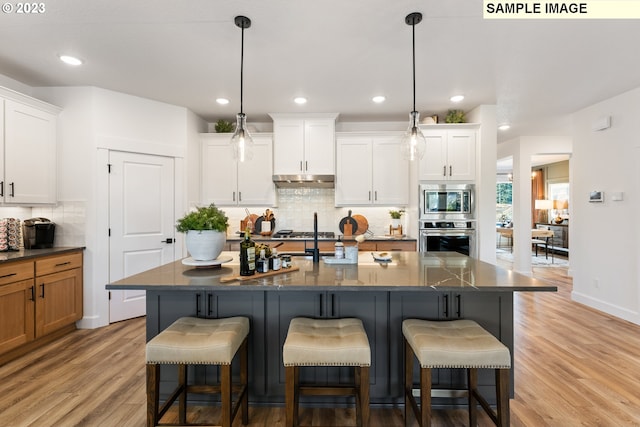 kitchen featuring stainless steel appliances, dark stone counters, a center island with sink, and white cabinets