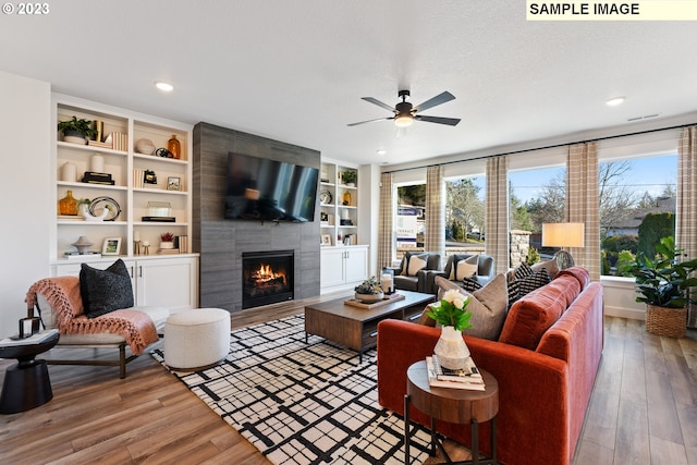 living room with ceiling fan, a tile fireplace, wood finished floors, and built in features