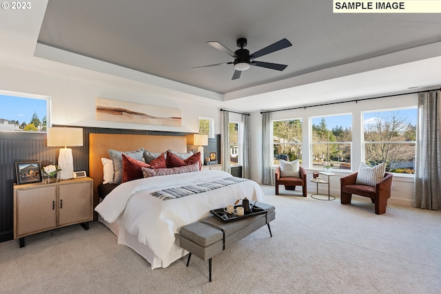 bedroom with light carpet, ceiling fan, and a raised ceiling