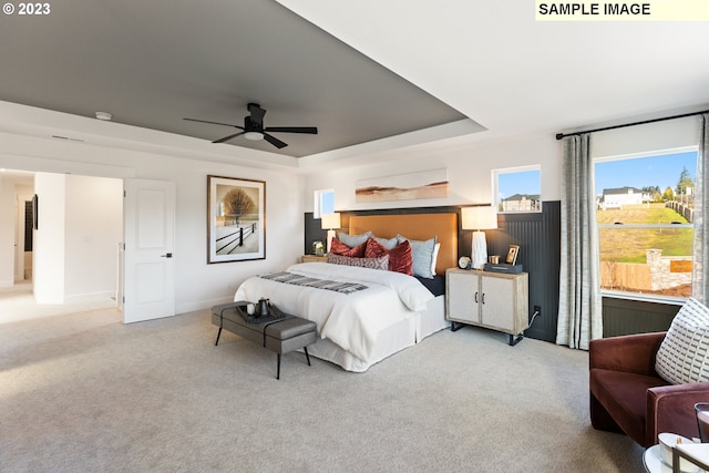 bedroom with a ceiling fan, a raised ceiling, light colored carpet, and baseboards