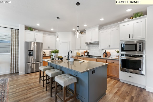 kitchen featuring tasteful backsplash, appliances with stainless steel finishes, a breakfast bar, light wood-style floors, and a sink