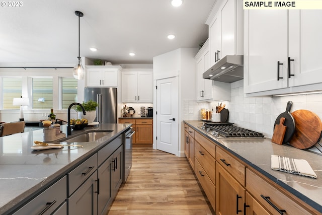 kitchen with light wood-style flooring, under cabinet range hood, a sink, appliances with stainless steel finishes, and dark stone counters