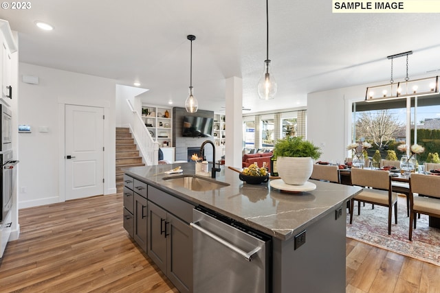 kitchen featuring appliances with stainless steel finishes, sink, dark stone countertops, a kitchen island with sink, and light hardwood / wood-style flooring