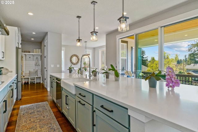 kitchen with stainless steel appliances, decorative light fixtures, light countertops, dark wood-style flooring, and a sink
