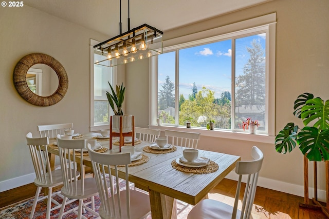 dining area with a wealth of natural light, wood finished floors, a notable chandelier, and baseboards