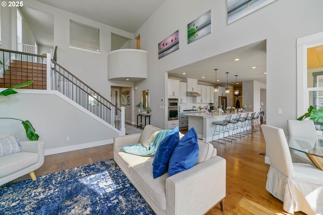 living area featuring stairway, wood finished floors, baseboards, and a high ceiling