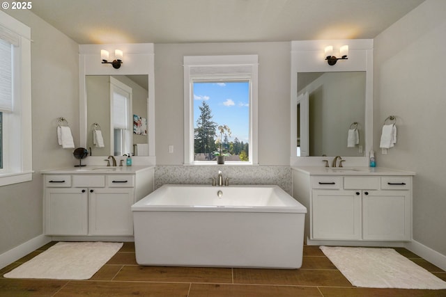 bathroom featuring a soaking tub, two vanities, wood finish floors, and a sink