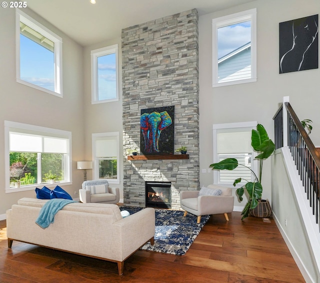living area featuring a towering ceiling, wood finished floors, and a stone fireplace