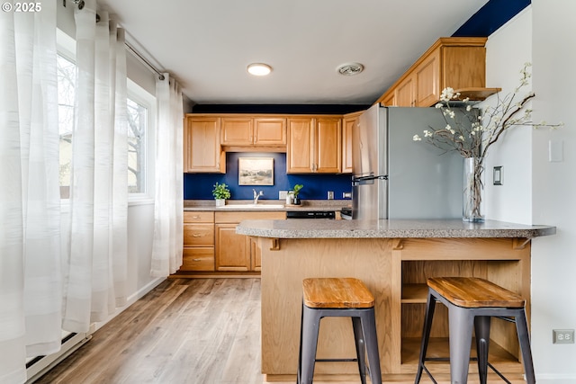 kitchen with a sink, a kitchen breakfast bar, freestanding refrigerator, light wood-style floors, and a peninsula