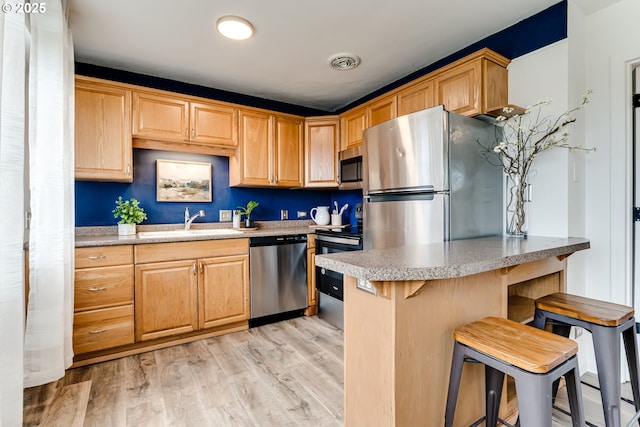 kitchen featuring visible vents, a kitchen bar, a sink, appliances with stainless steel finishes, and light wood finished floors