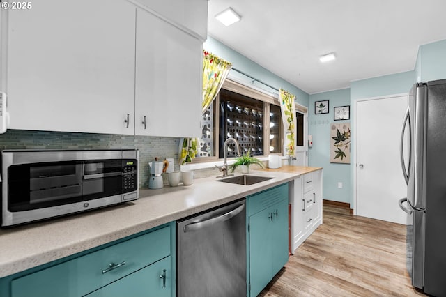 kitchen featuring appliances with stainless steel finishes, a sink, light countertops, light wood-style floors, and backsplash