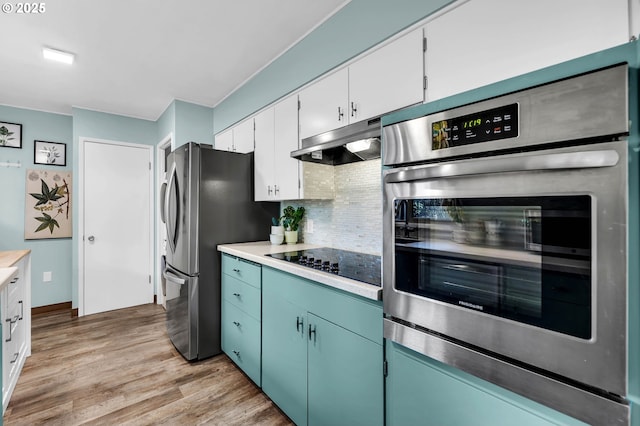 kitchen with under cabinet range hood, stainless steel appliances, light countertops, decorative backsplash, and light wood finished floors