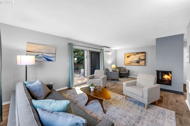 living area featuring a lit fireplace, baseboards, wood finished floors, and a wall mounted air conditioner