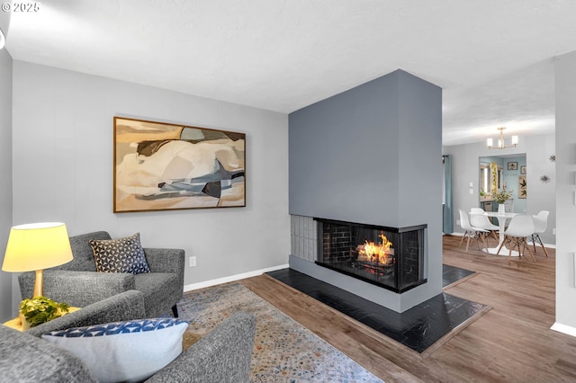 living area with baseboards, a multi sided fireplace, and wood finished floors