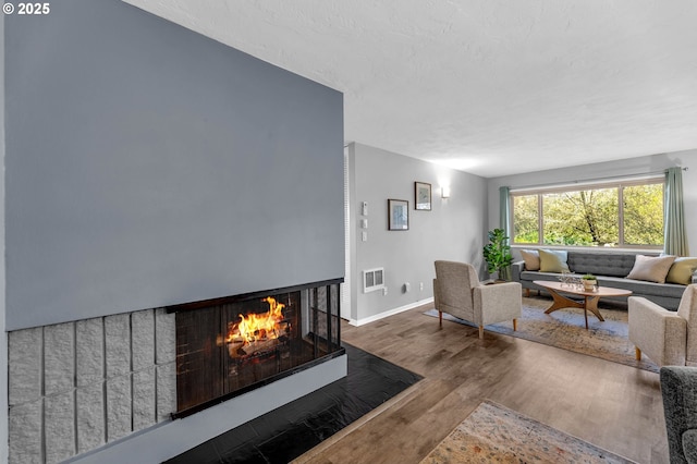 living area featuring visible vents, a multi sided fireplace, a textured ceiling, wood finished floors, and baseboards