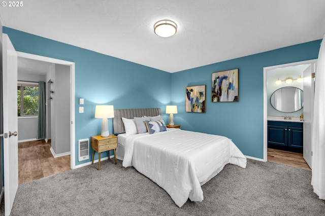 bedroom with carpet floors, heating unit, a sink, ensuite bath, and baseboards