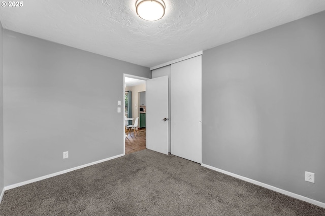 unfurnished bedroom with carpet, a closet, a textured ceiling, and baseboards