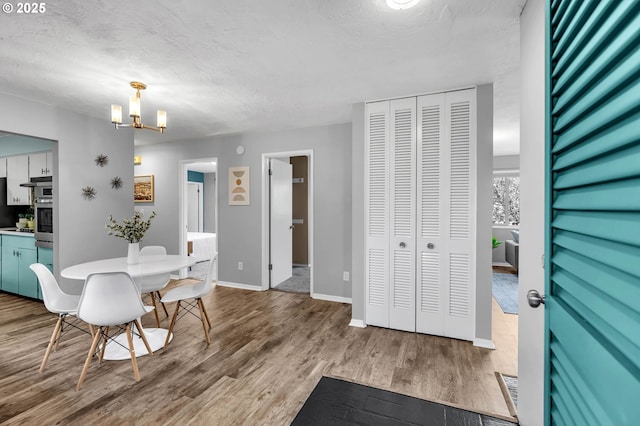 dining room featuring a notable chandelier, a textured ceiling, baseboards, and wood finished floors