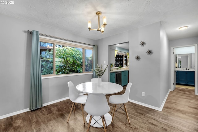 dining space featuring a chandelier, a textured ceiling, wood finished floors, and baseboards