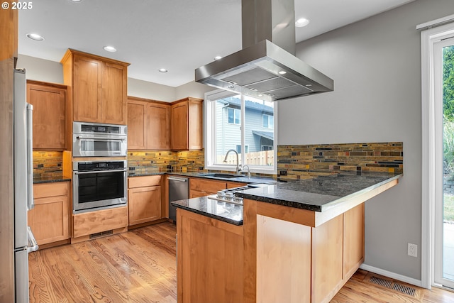 16099 SE Venice Ridge Way, Damascus, OR 97089 - kitchen featuring island exhaust hood, a peninsula, decorative backsplash, stainless steel appliances, and light wood finished floors