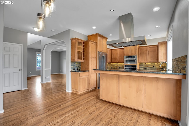 16099 SE Venice Ridge Way, Damascus, OR 97089 - kitchen with island exhaust hood, light wood finished floors, glass insert cabinets, backsplash, and appliances with stainless steel finishes
