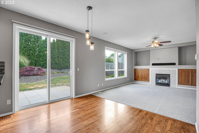 16099 SE Venice Ridge Way, Damascus, OR 97089 - unfurnished living room with a tiled fireplace, wood finished floors, a ceiling fan, and built in shelves