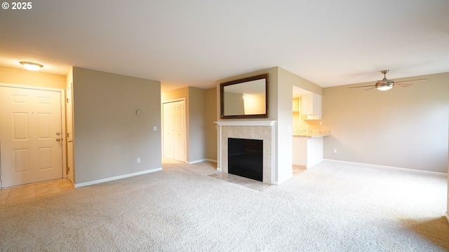 unfurnished living room with ceiling fan, baseboards, a tiled fireplace, and light colored carpet