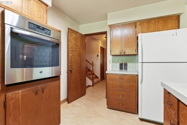 kitchen with light countertops, freestanding refrigerator, stainless steel oven, and brown cabinetry