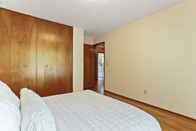 bedroom featuring a textured ceiling, baseboards, a closet, and wood finished floors