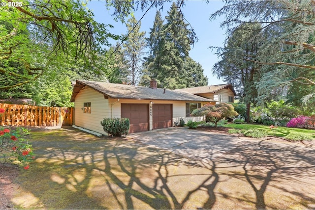 view of front of house featuring an attached garage, fence, driveway, and a chimney