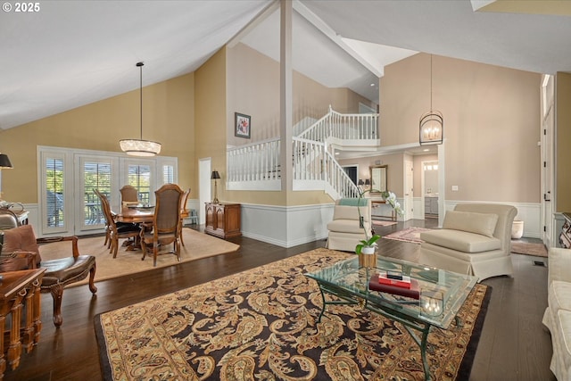 living room featuring high vaulted ceiling, hardwood / wood-style flooring, a wainscoted wall, a chandelier, and stairs