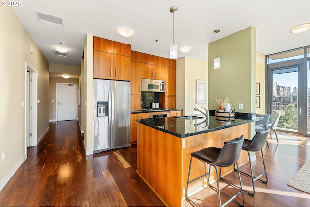 kitchen with visible vents, appliances with stainless steel finishes, brown cabinetry, a sink, and a kitchen breakfast bar