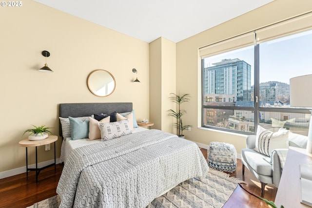 bedroom featuring a view of city, multiple windows, wood finished floors, and baseboards