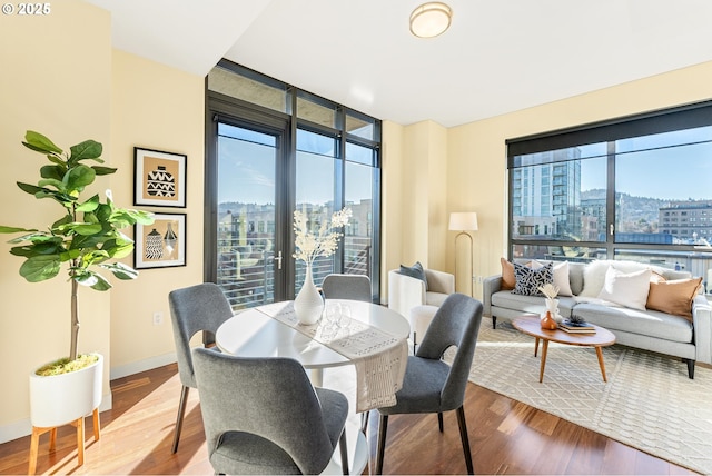 dining room with baseboards, a wall of windows, wood finished floors, and a city view