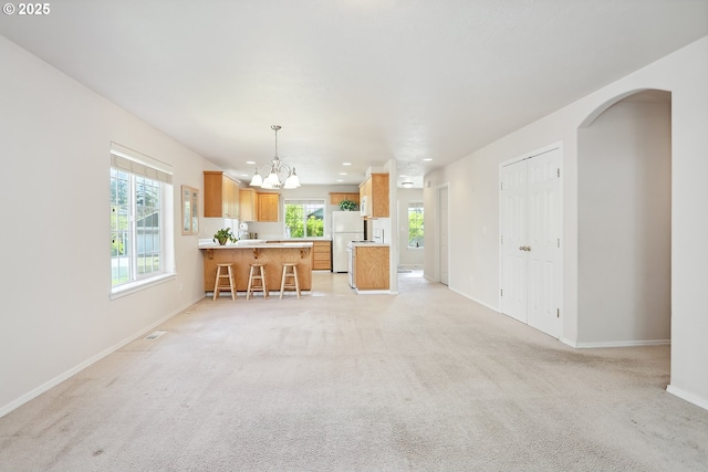 unfurnished living room with recessed lighting, an inviting chandelier, light carpet, baseboards, and arched walkways