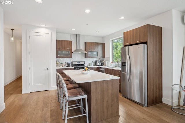 kitchen with a kitchen island, a breakfast bar, wall chimney exhaust hood, a sink, and stainless steel appliances