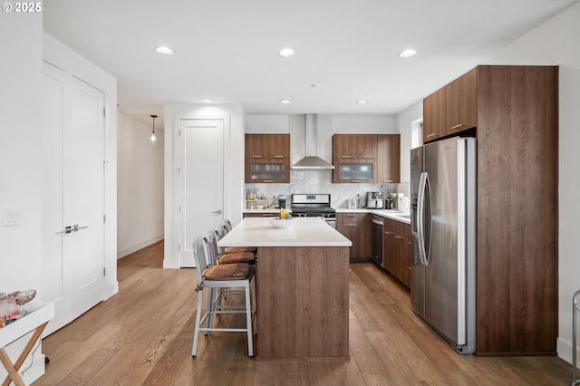 kitchen with light wood-type flooring, wall chimney exhaust hood, appliances with stainless steel finishes, and a breakfast bar area