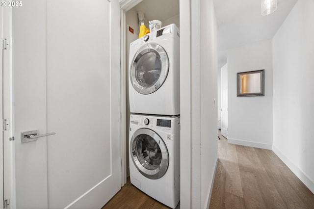 laundry room featuring stacked washing maching and dryer, baseboards, laundry area, and wood finished floors