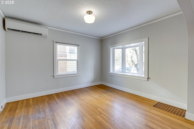 unfurnished room with hardwood / wood-style floors, ornamental molding, an AC wall unit, and a textured ceiling