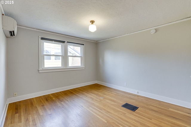 empty room with wood-type flooring, a wall mounted air conditioner, and a textured ceiling