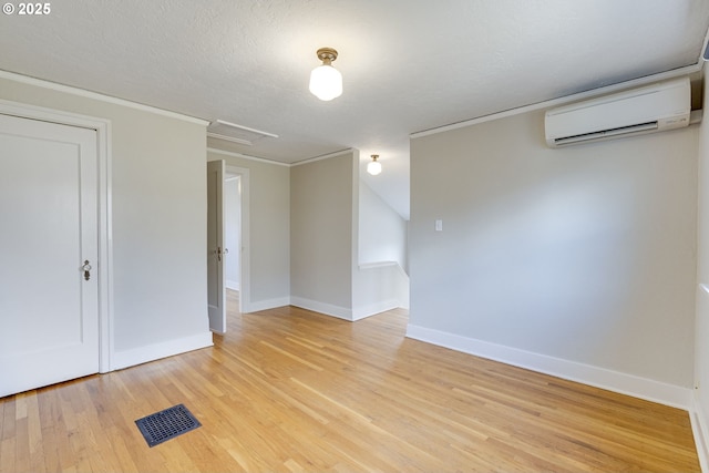 spare room featuring crown molding, a wall mounted AC, light hardwood / wood-style floors, and a textured ceiling